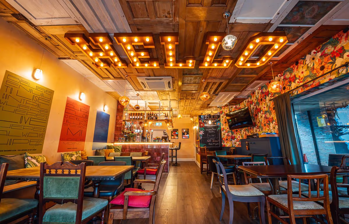 A bright and colourful bar/restaurant sits empty. The word hello is spelled out in large lights on the ceiling