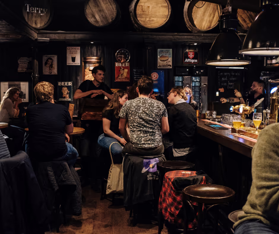 A group of people enjoying drinks while seated at a bar in a lively pub atmosphere.