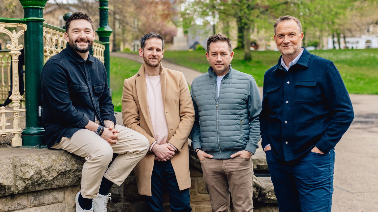 A group of four men smile into the camera for a photo, three of them have hands in the pockets of their jackets