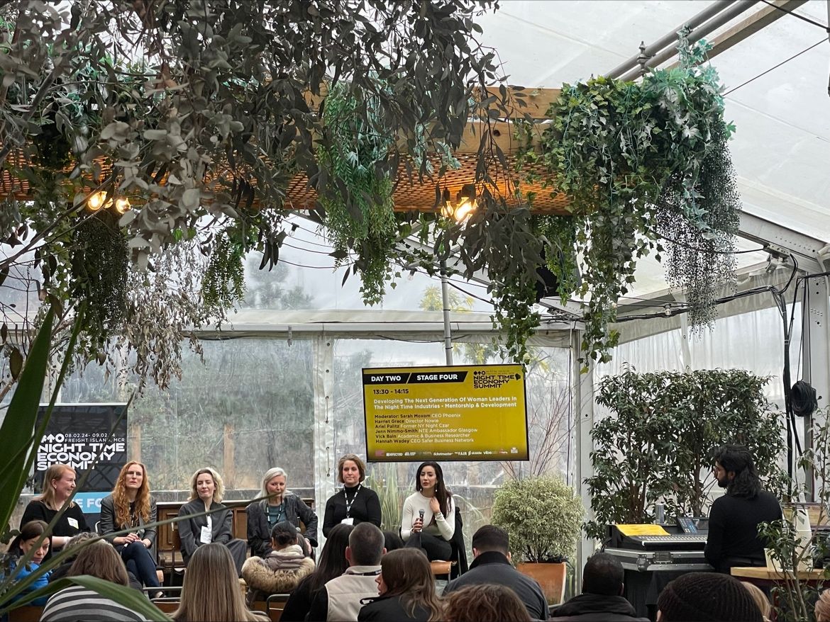 People gathered in a tent, surrounded by plants suspended from the ceiling, fostering a warm and inviting environment