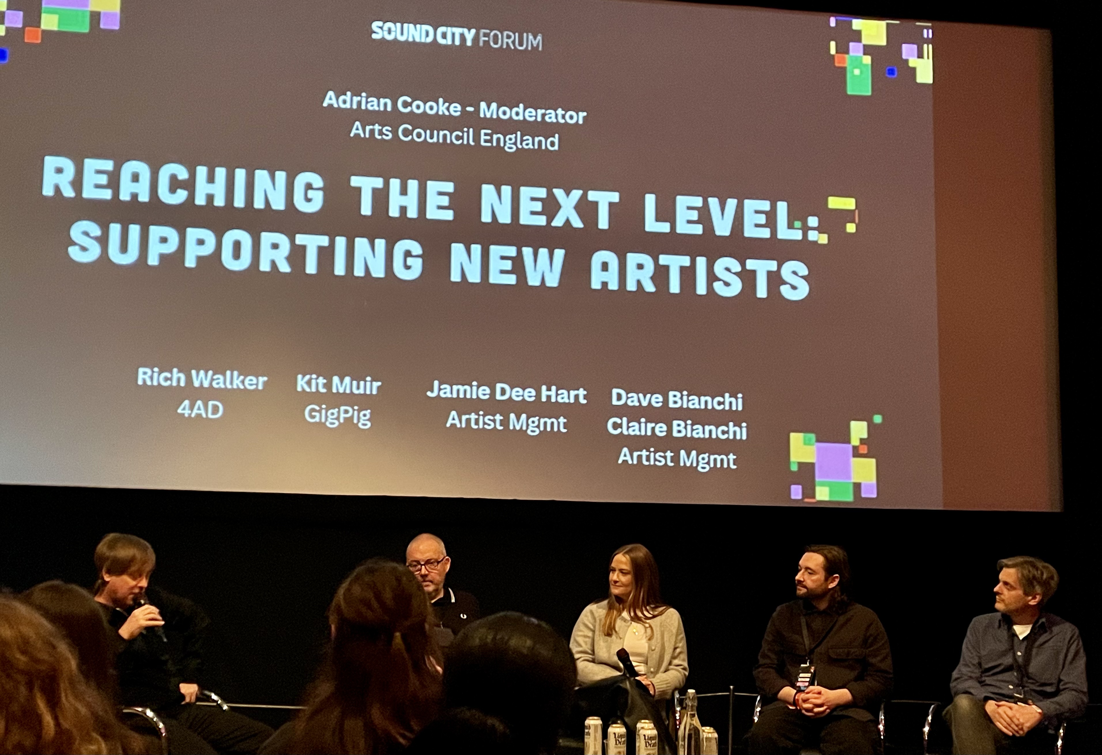 A group of five people are on a stage holding microphones as they are being interviewed for a panel 