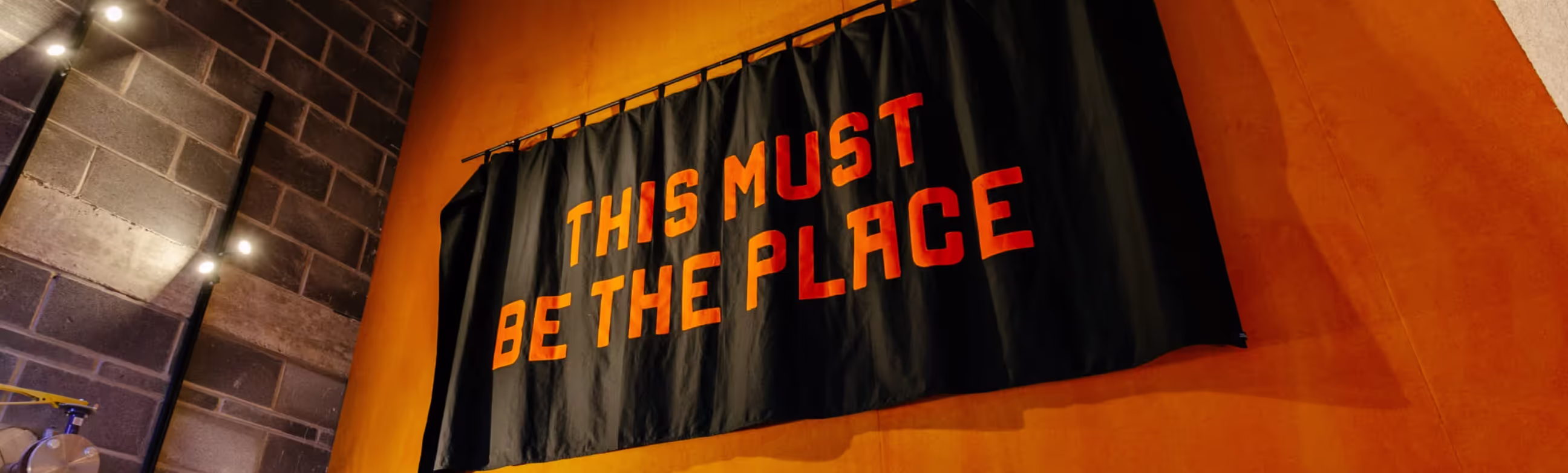 An orange wall with a large black banner stating "This must be the place"