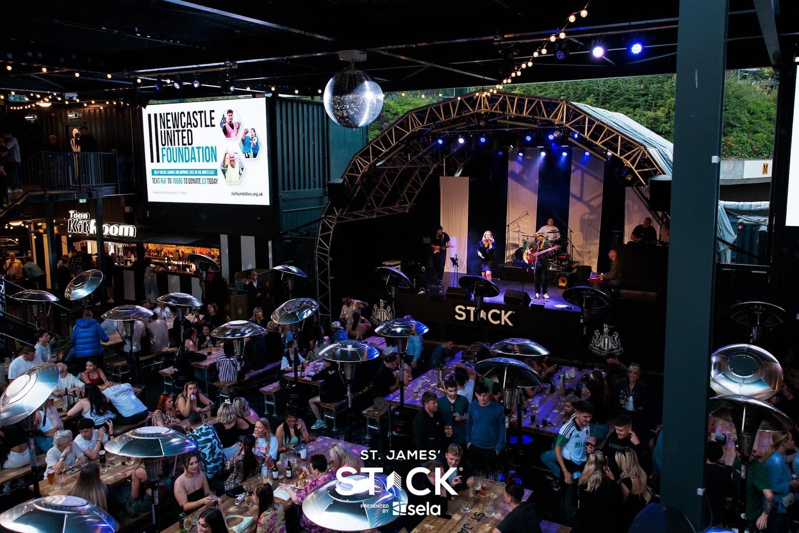 Image taken in Stack, with tables surrounded by people and a stage in the centre of the image with a performer and band