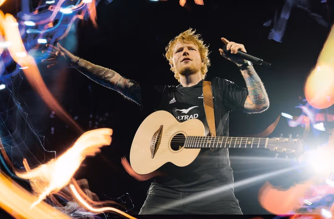 A shot of Ed Sheeran holding a guitar and a microphone as he sings to fans at a concert