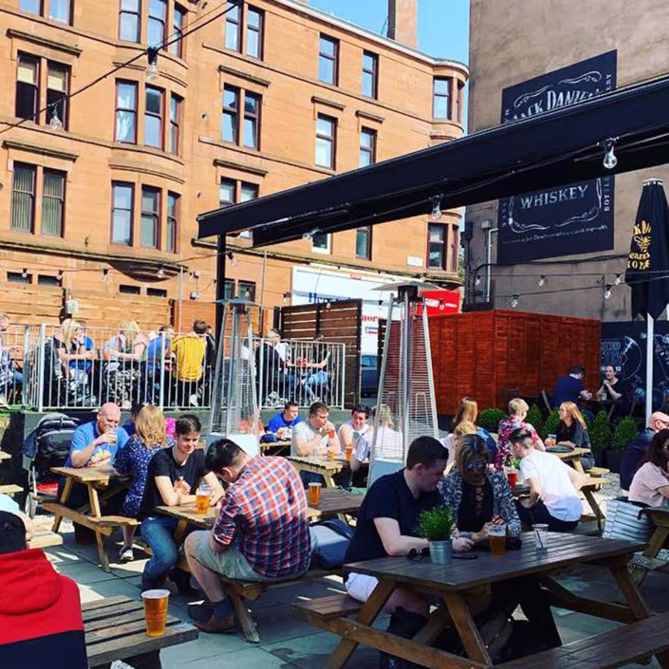 A beer garden with wooden tables captured on a sunny day, with customers engaged in friendly conversation