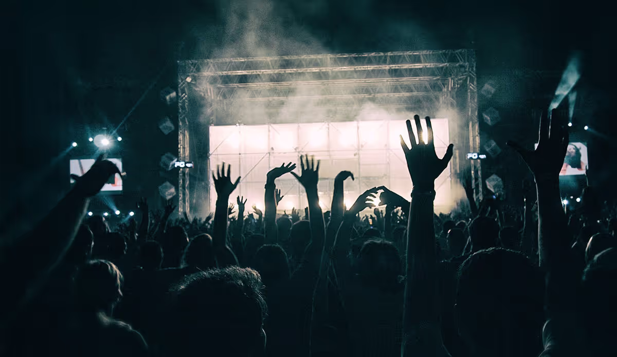 A black and white shot of a large crowd enjoying live music at a concert with their hands raised in excitement