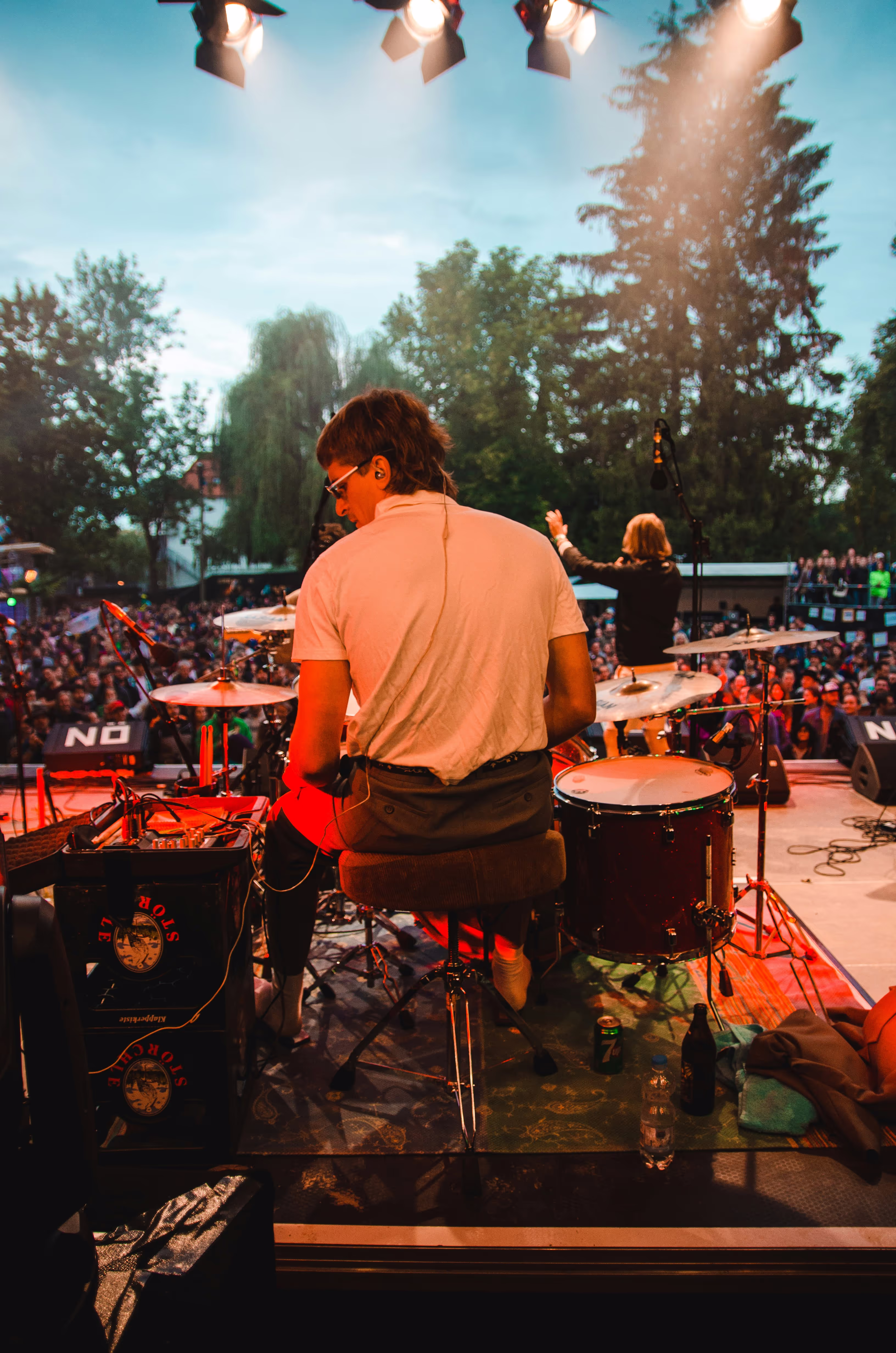 A drummer is on stage performing in front of a crowd at a dimly lit festival