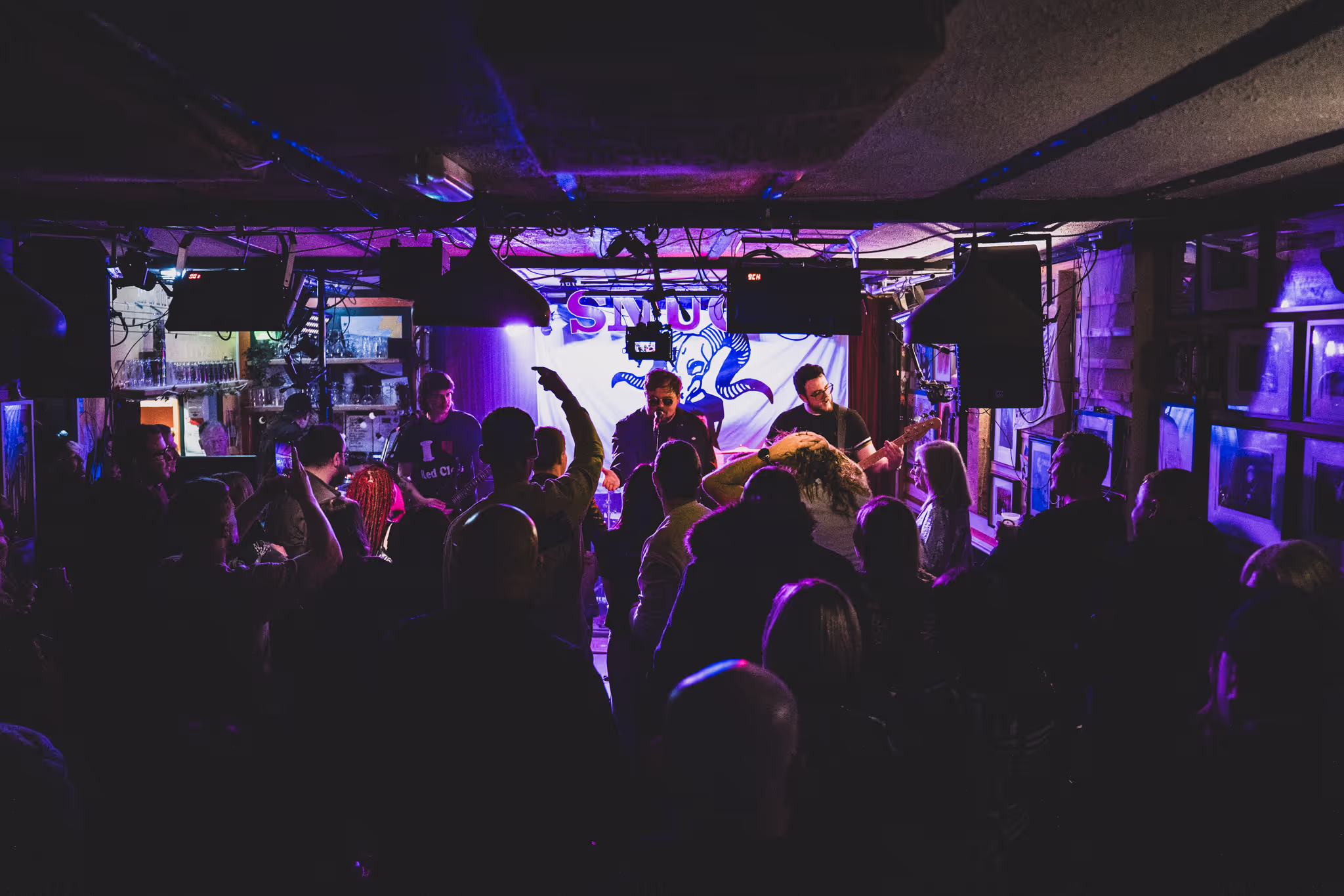 A band perform in front of a crowd in a dimly lit room