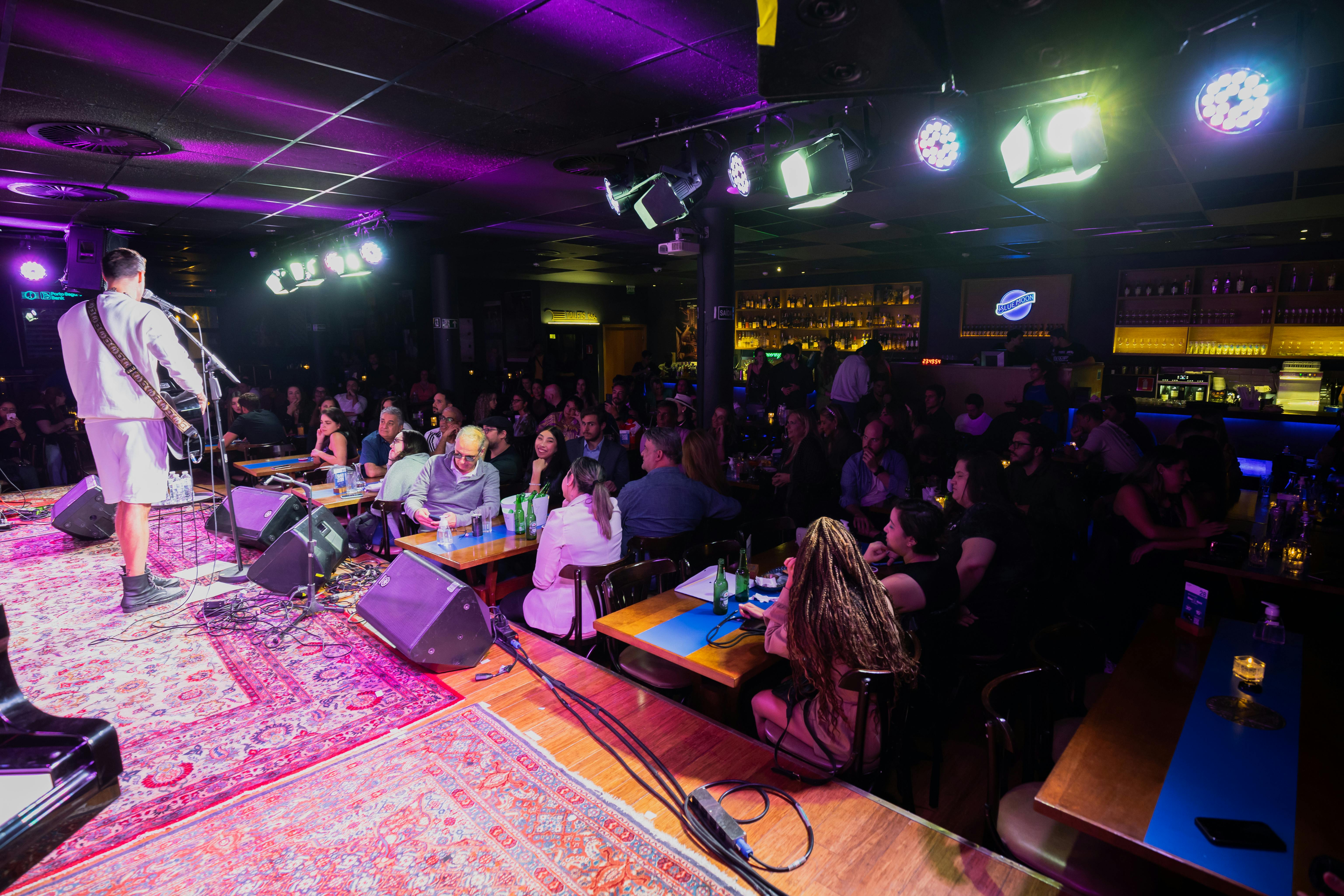 A man performs to an audience on a stage covered with decorative rugs.