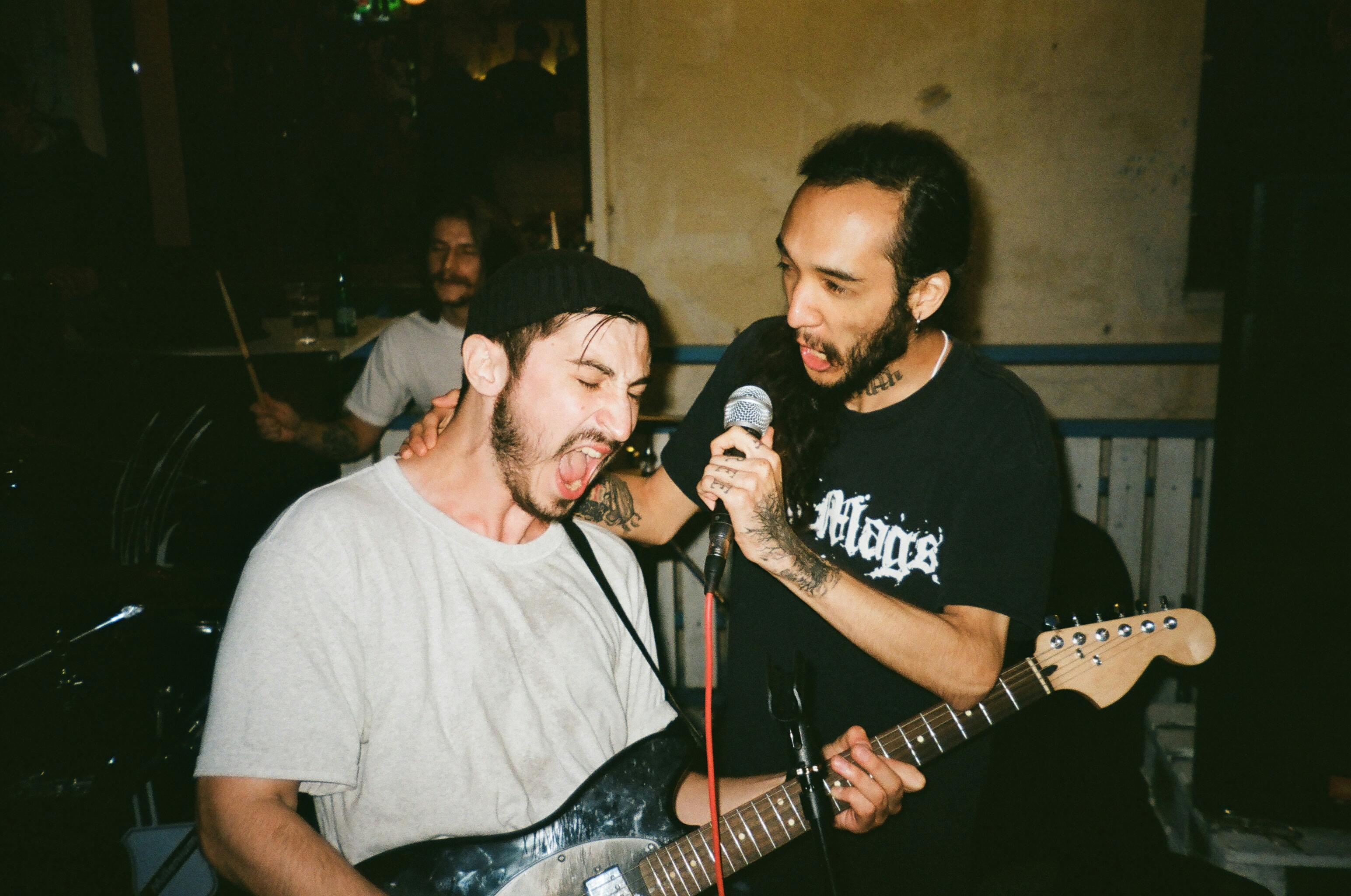 Two men singing whilst playing guitar in a band