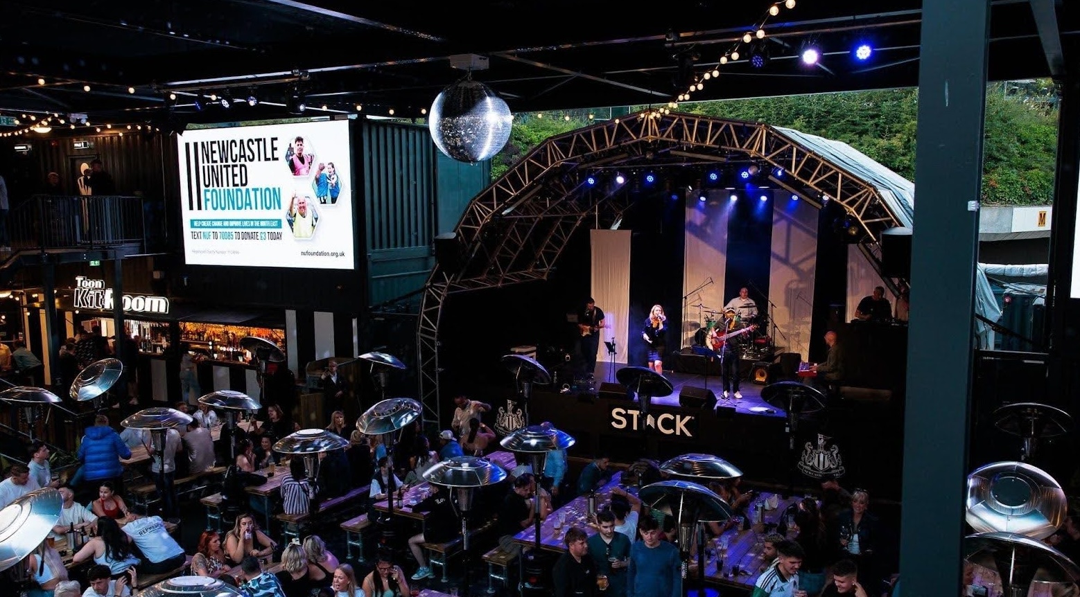A band playing on a stage at STACK St James' Park to a room full of guests