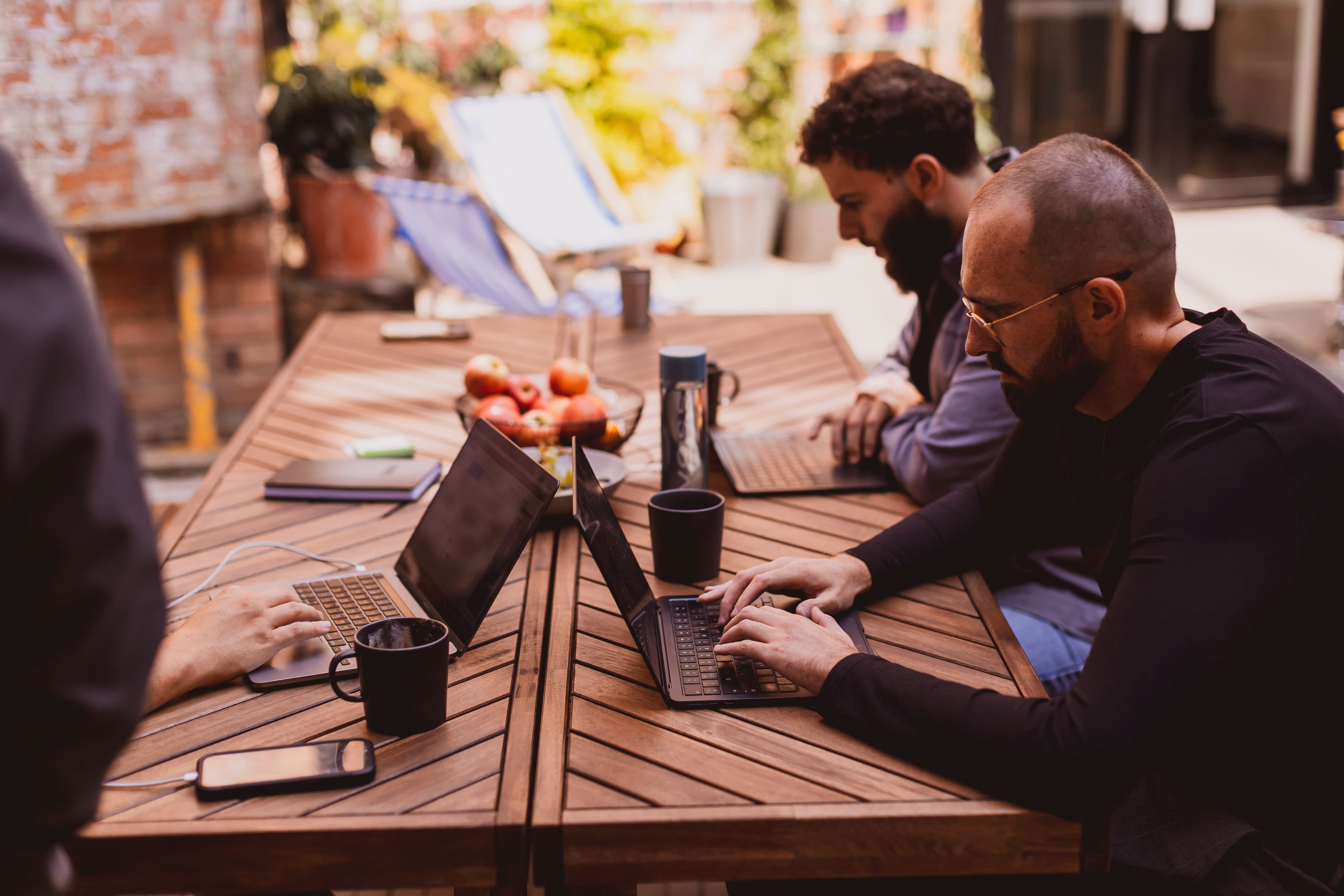 Kubix team members working on laptops around an outdoor wooden table