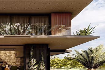 Modern concrete building with large glass windows and overhanging balconies surrounded by various green plants and trees.