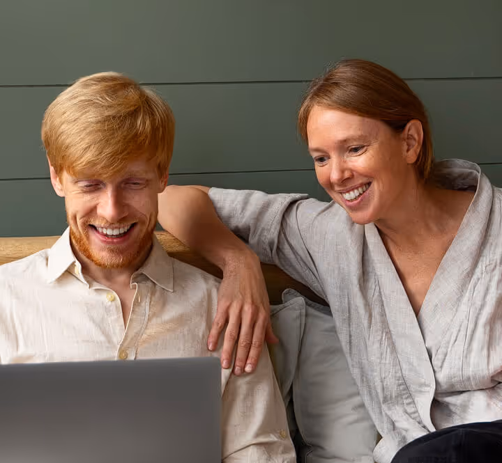 Smiling man and woman sitting closely together looking at a laptop screen.