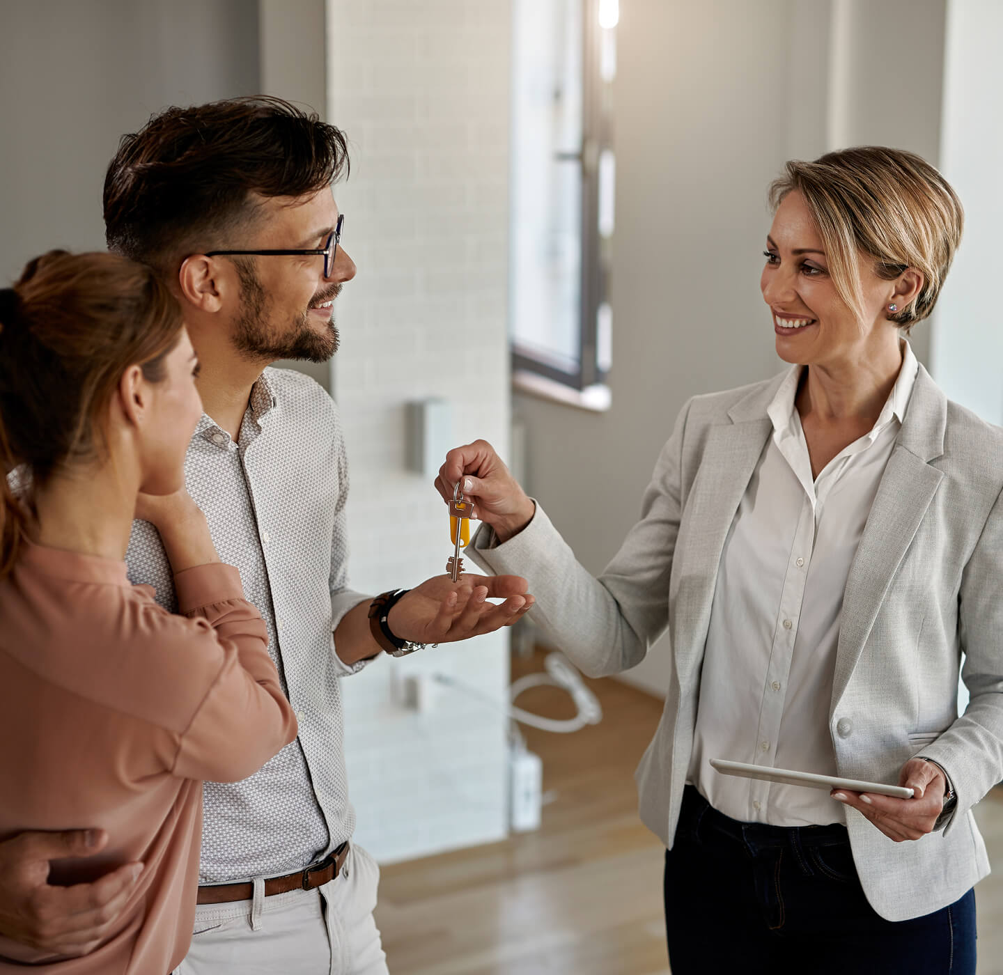 Real estate agent handing house keys to a smiling couple inside a bright home.