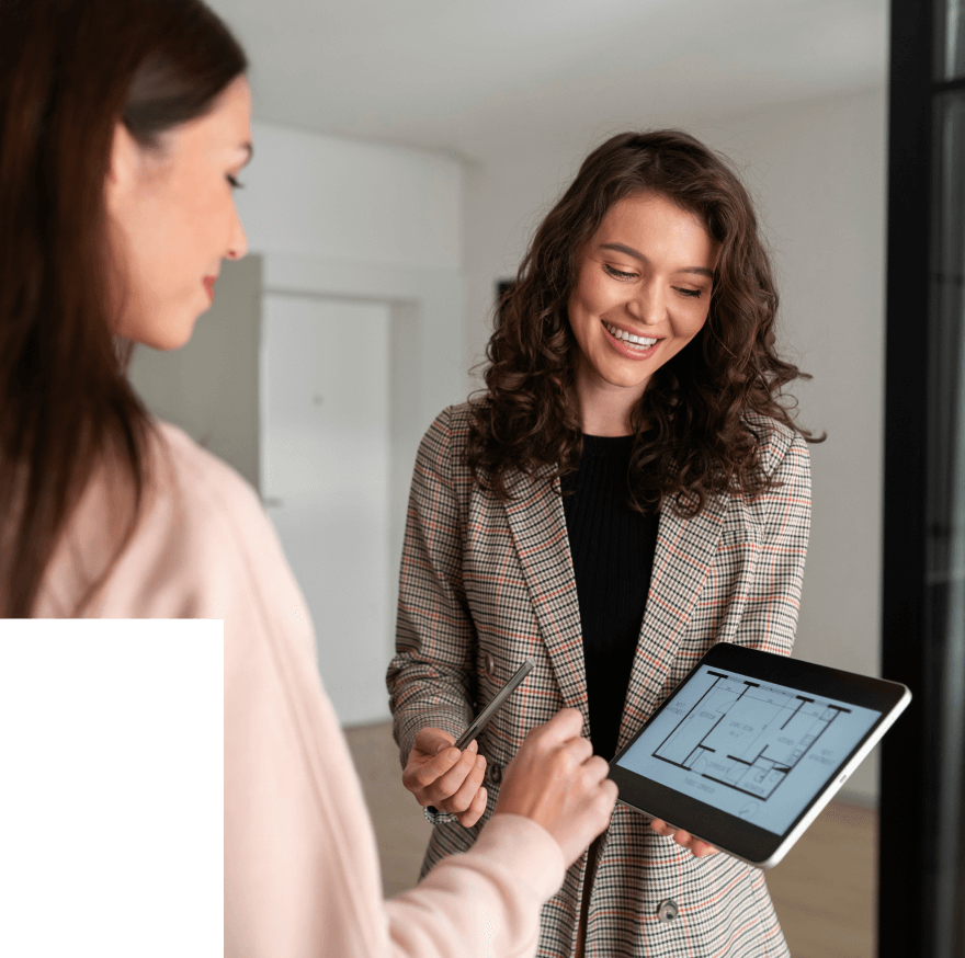 Two women discussing a building floor plan displayed on a tablet, one pointing with a pen.
