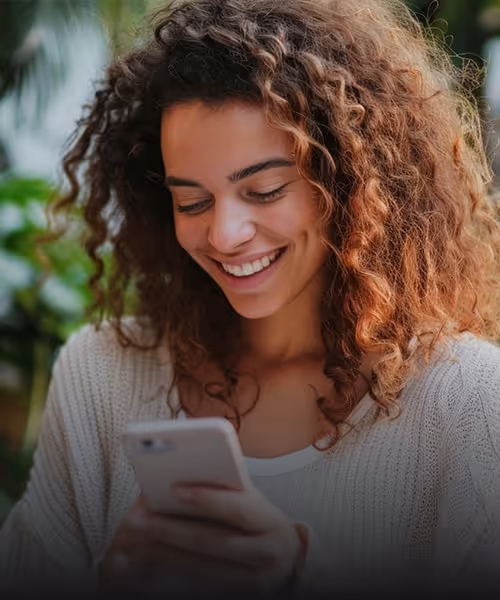 Visual for slide: young woman with curly hair smiling while looking at her smartphone outdoors.