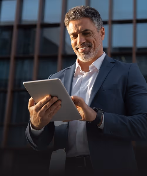 Visual for slide: smiling middle-aged man in a suit using a tablet outdoors in front of a glass building.