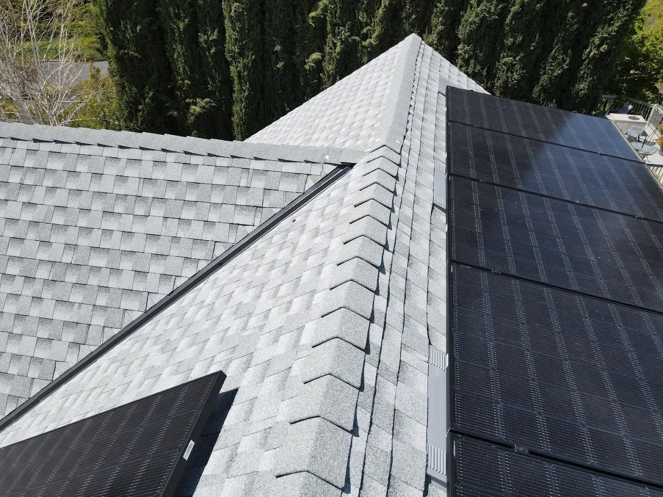 Light gray shingled rooftop with black solar panels installed on two sections.