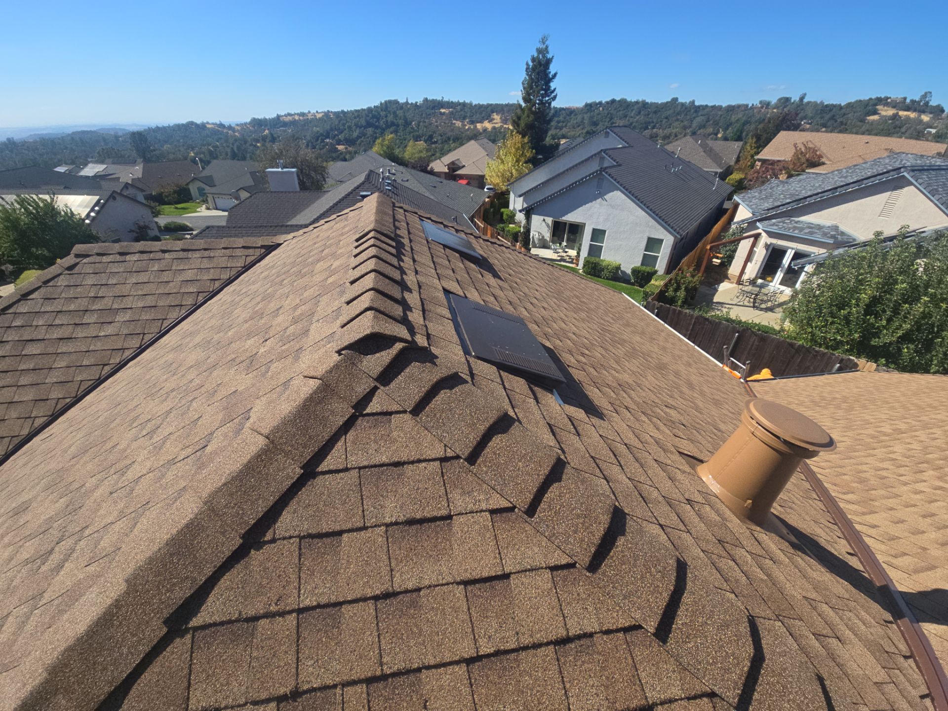 View of brown shingled rooftops in a residential neighborhood under a clear blue sky.