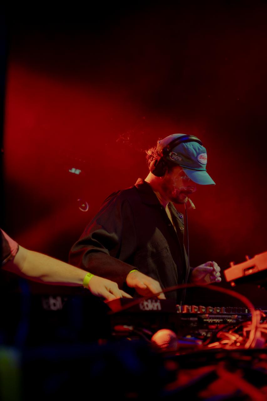 DJ portant une casquette et un casque, concentré sur la table de mixage entourée de lumière rouge.