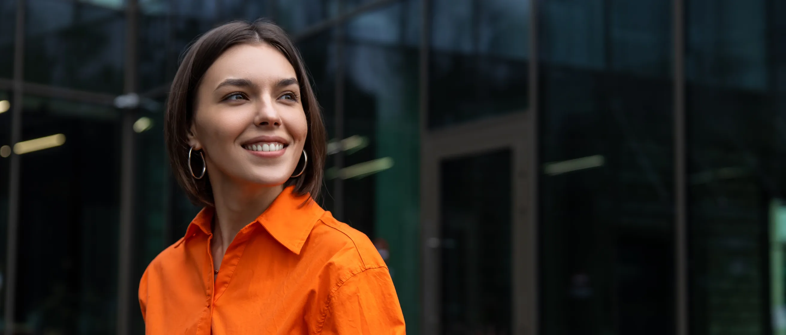 Homem sorridente de moletom laranja sentado em poltrona, usando smartphone. Ao fundo, telas flutuantes exibem gráficos de desempenho e sessões agendadas, em estilo moderno e digital.