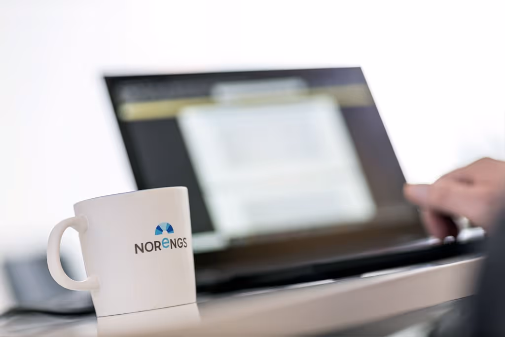 Laptop med händer som skriver på tangentbord bredvid vit kaffekopp med Norengs logotyp - Modern redovisning och bokföring Gävle