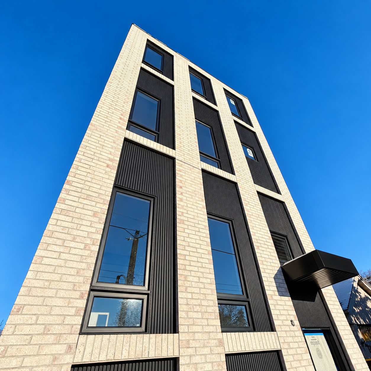 Low-angle view of Leaside 1's light brick facade, black window trim, and entrance canopy against a blue sky.