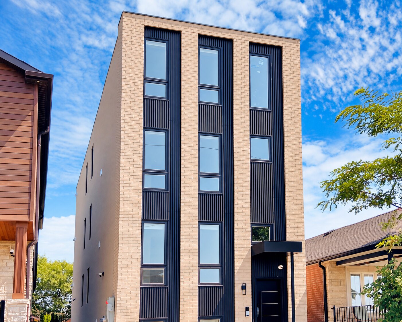 Front view of Fairbank 1's light brick facade with black vertical cladding and window trim.