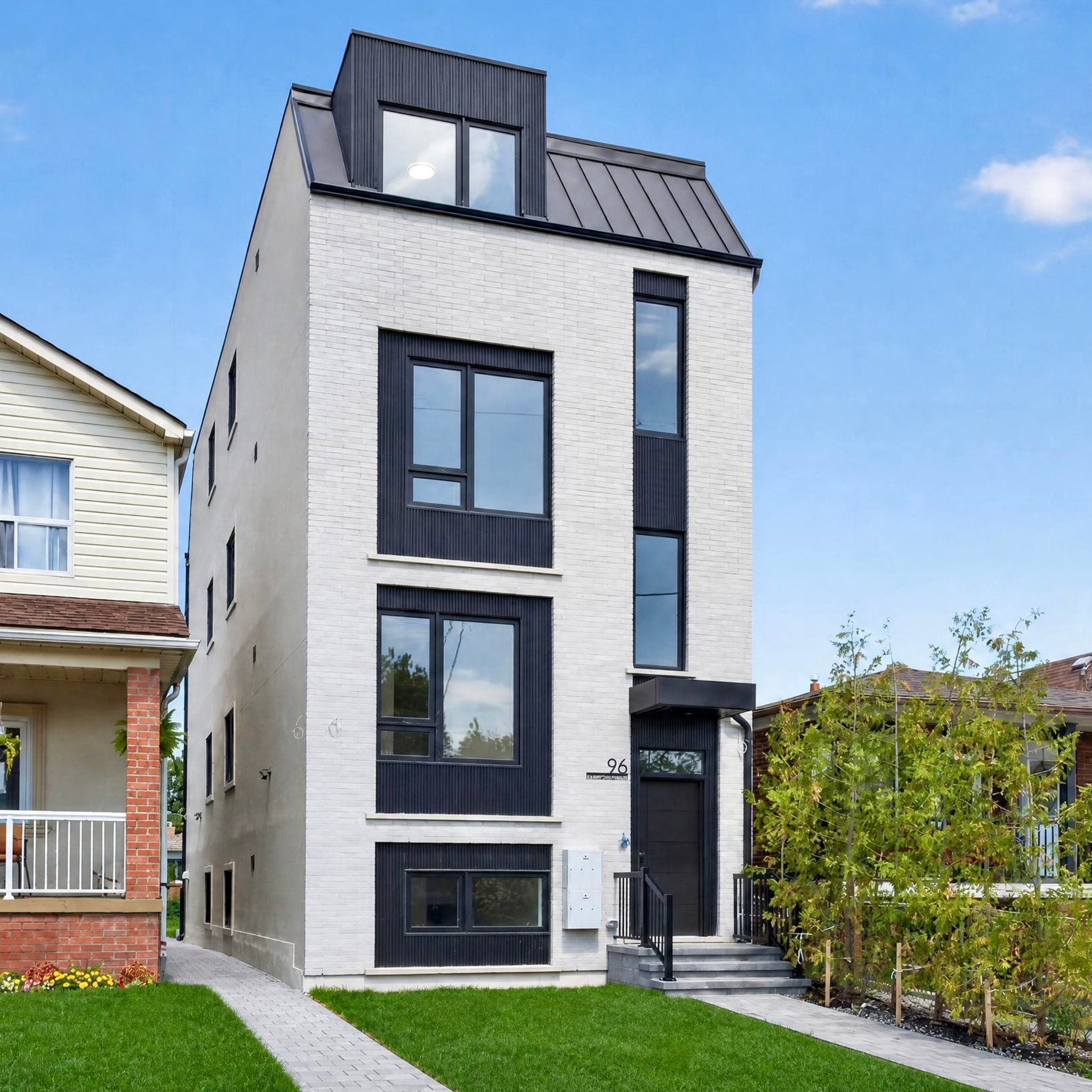 Angled view of a light brick residential building with black window trim, a dormer window, and front steps.