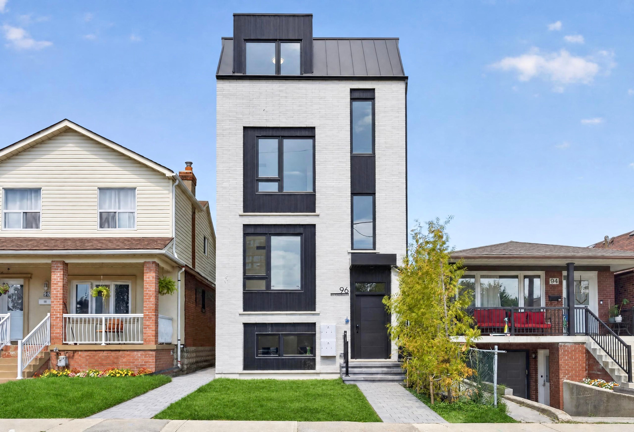 Front view of a light brick residential building with black window trim, a dormer window, and a lawn.