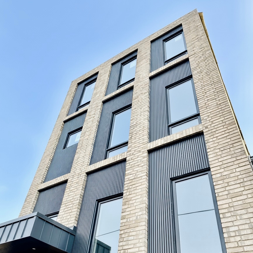Low-angle view of St. Clair West 1's light brick facade, black vertical window panels, and entrance canopy.