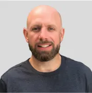 Professional headshot of a smiling man with a beard wearing a dark gray t-shirt against a light background