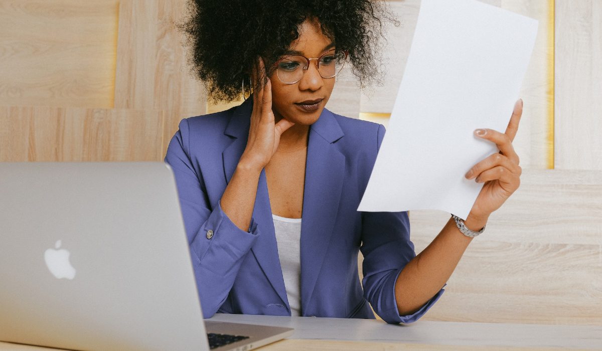 Mulher observa documento impresso em frente a computador