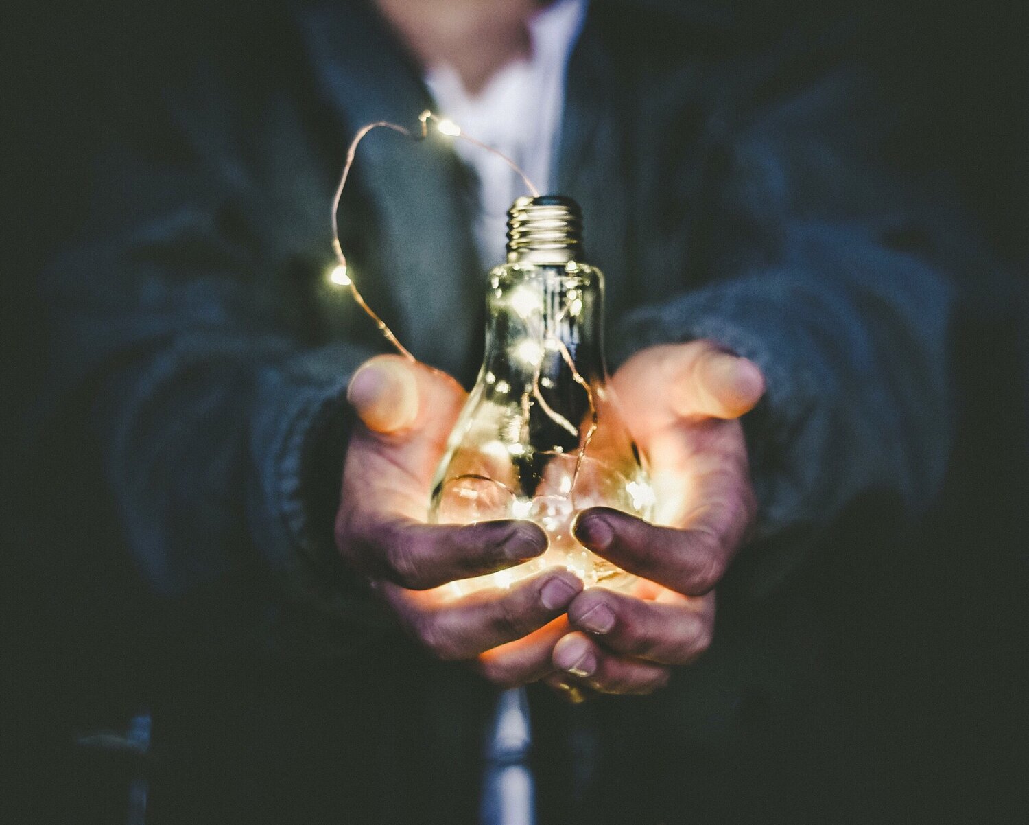 Person cupping a glowing light bulb filled with fairy lights
