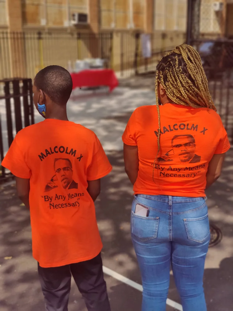 Two students wearing orange Malcolm X By Any Means Necessary shirts