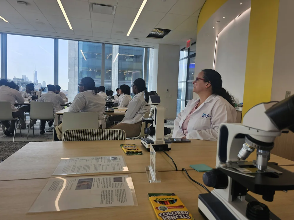 Students in lab coats using microscopes during Pfizer science workshop
