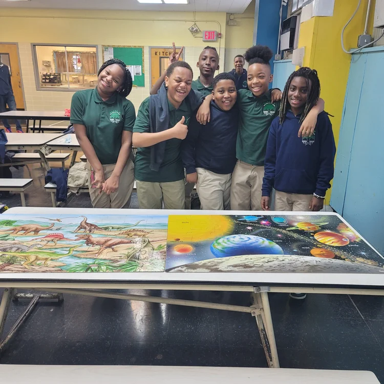 Students in uniforms posing with dinosaur and solar system posters
