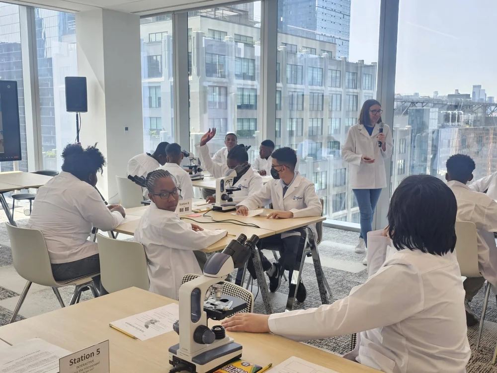 Students in lab coats use microscopes during a science workshop