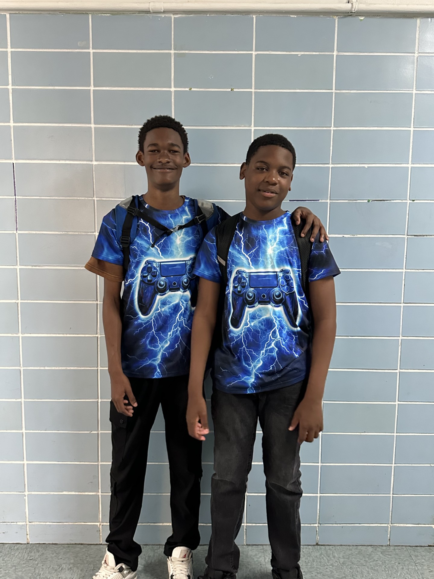 Two students wearing matching gaming shirts pose in school hallway