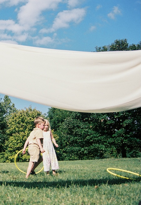 Two children play with yellow hoops under a white canopy on a summer lawn