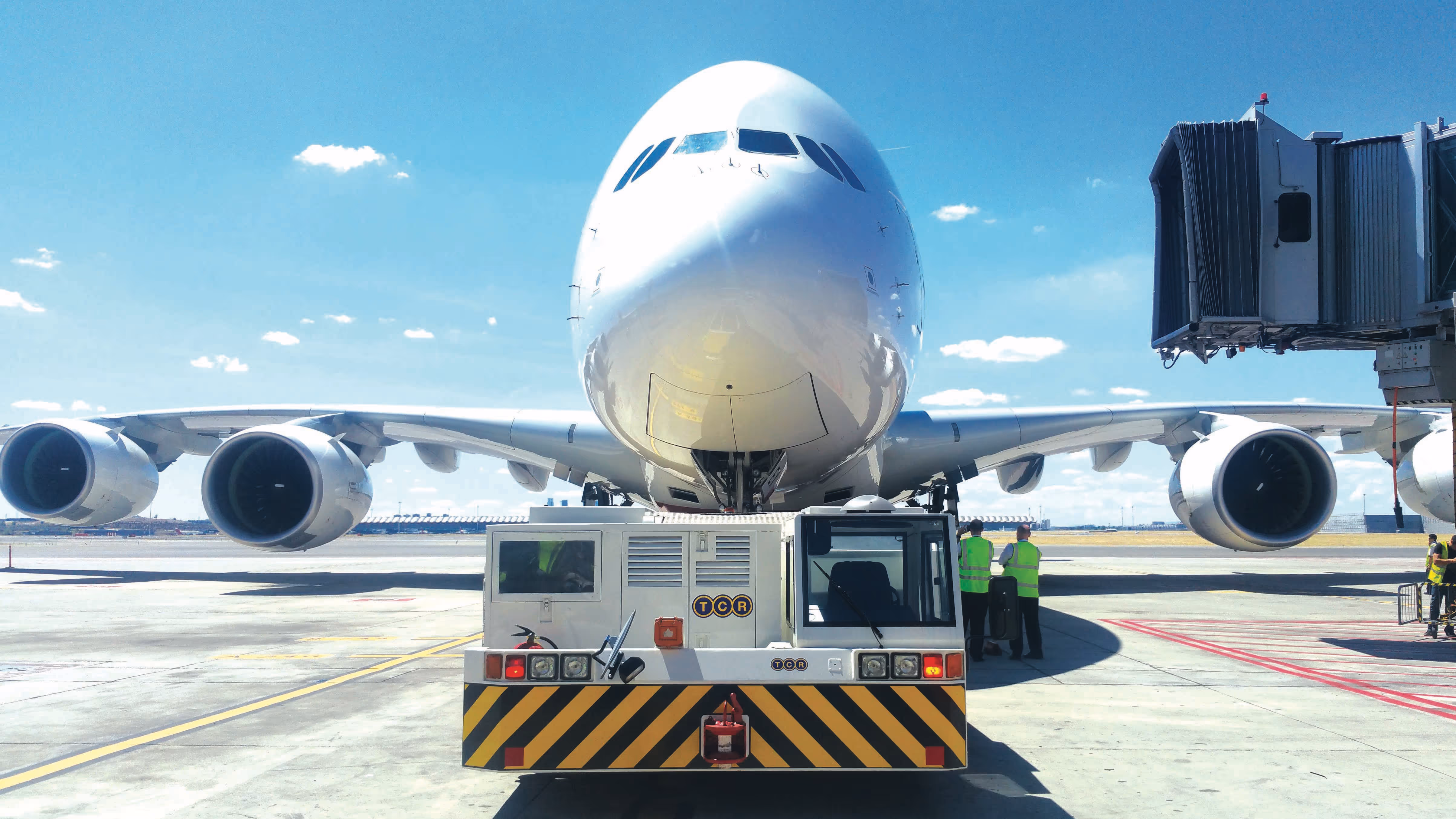 Front view of a large commercial airplane connected to a pushback tug at an airport gate on a clear day.