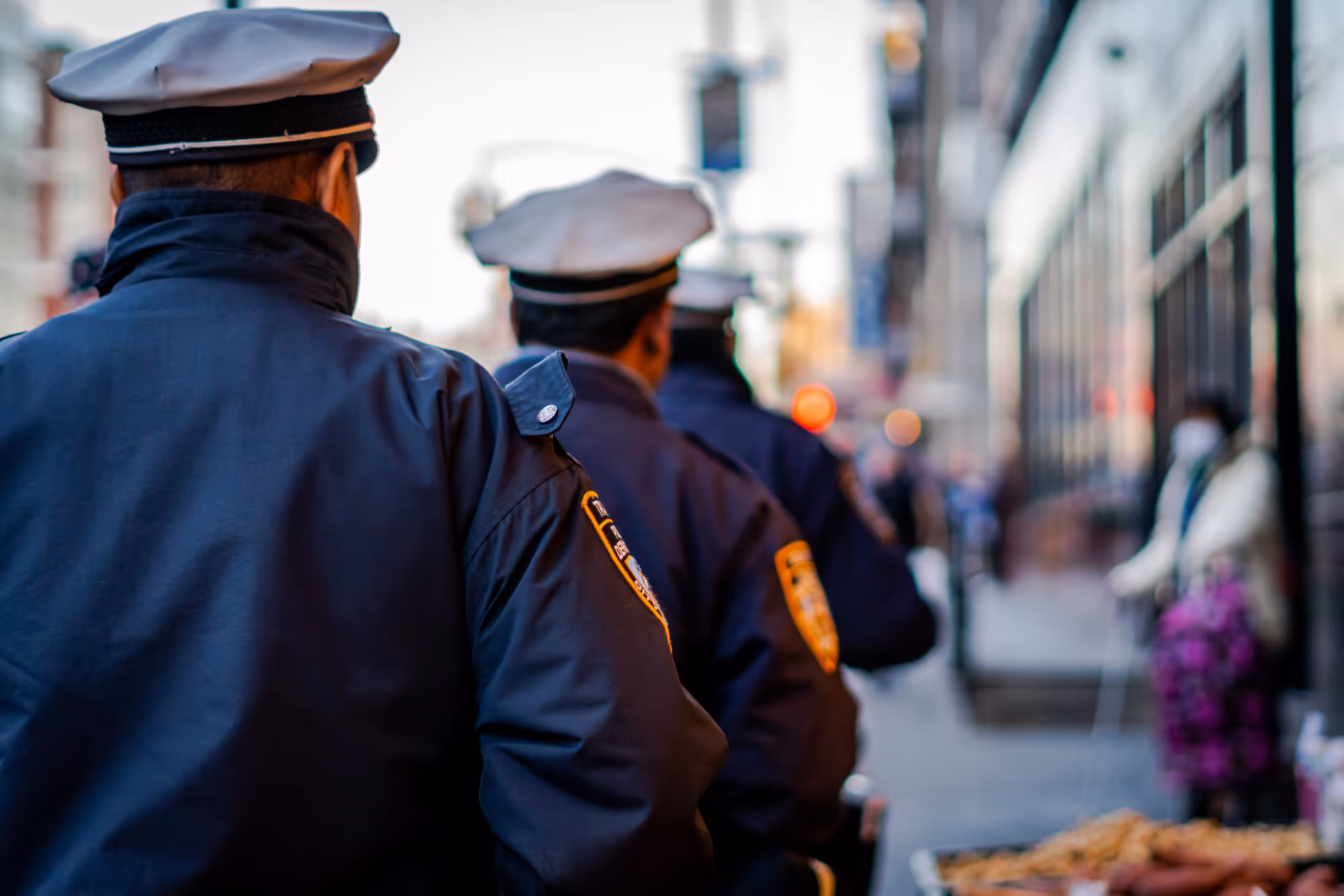 Three police officers standing with their backs facing the camera on a city street.