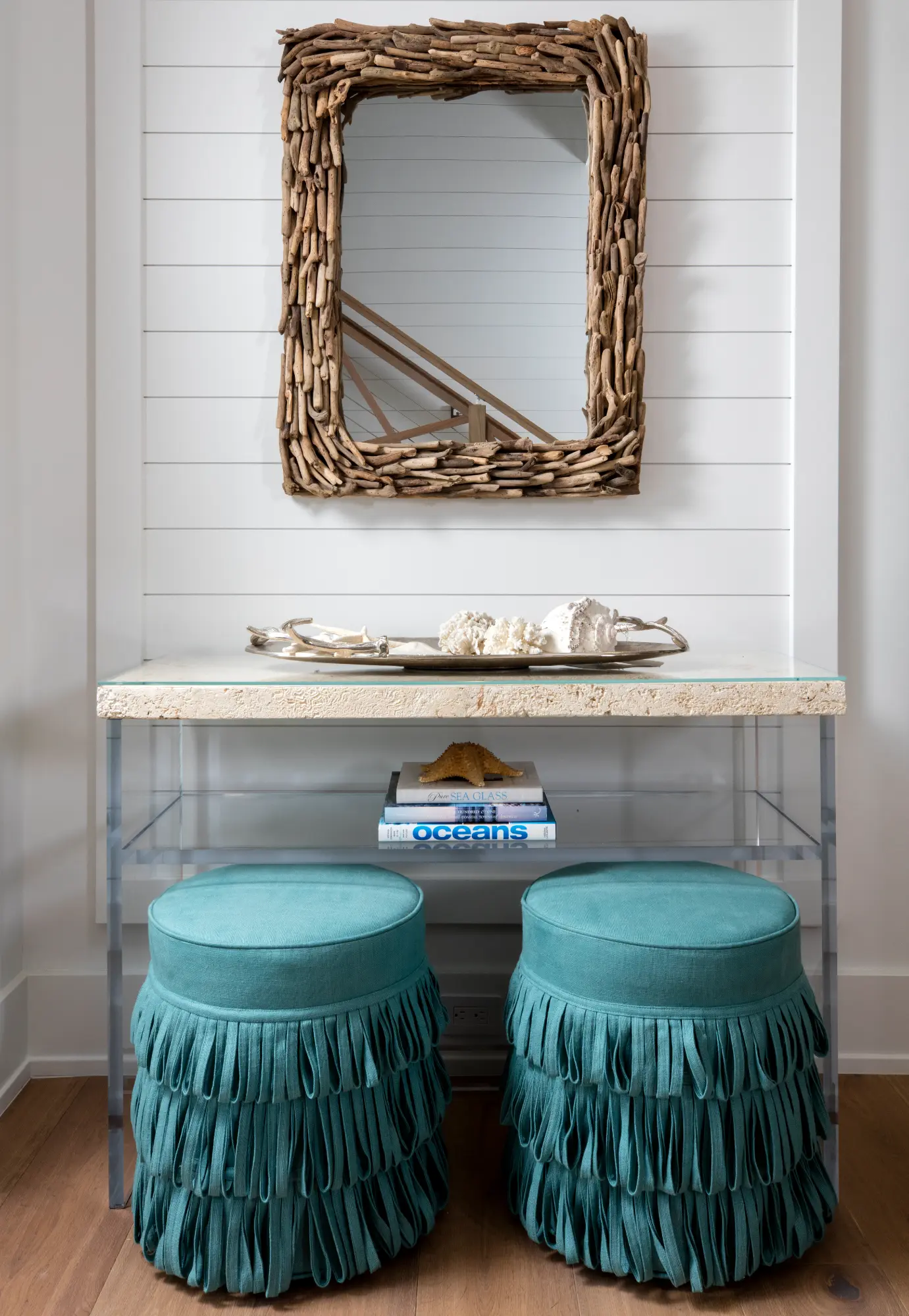 A decorative mirror hangs above a table with two teal fringed stools underneath.