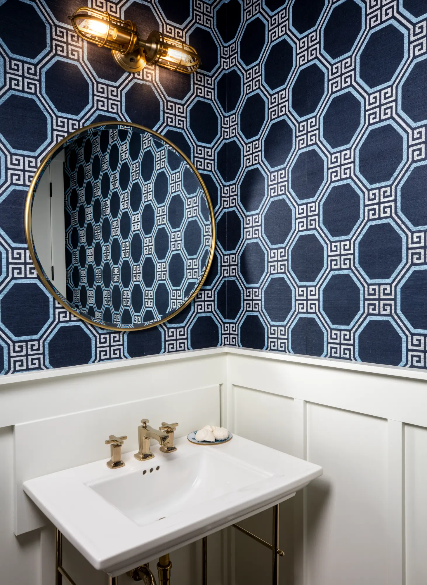 A bathroom with octagonal patterned wallpaper, a round mirror, and a white sink.