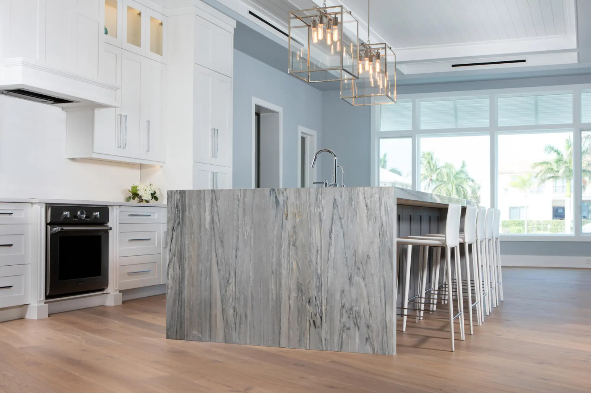 A modern kitchen with a large marble island and high chairs, set under geometric pendant lights.