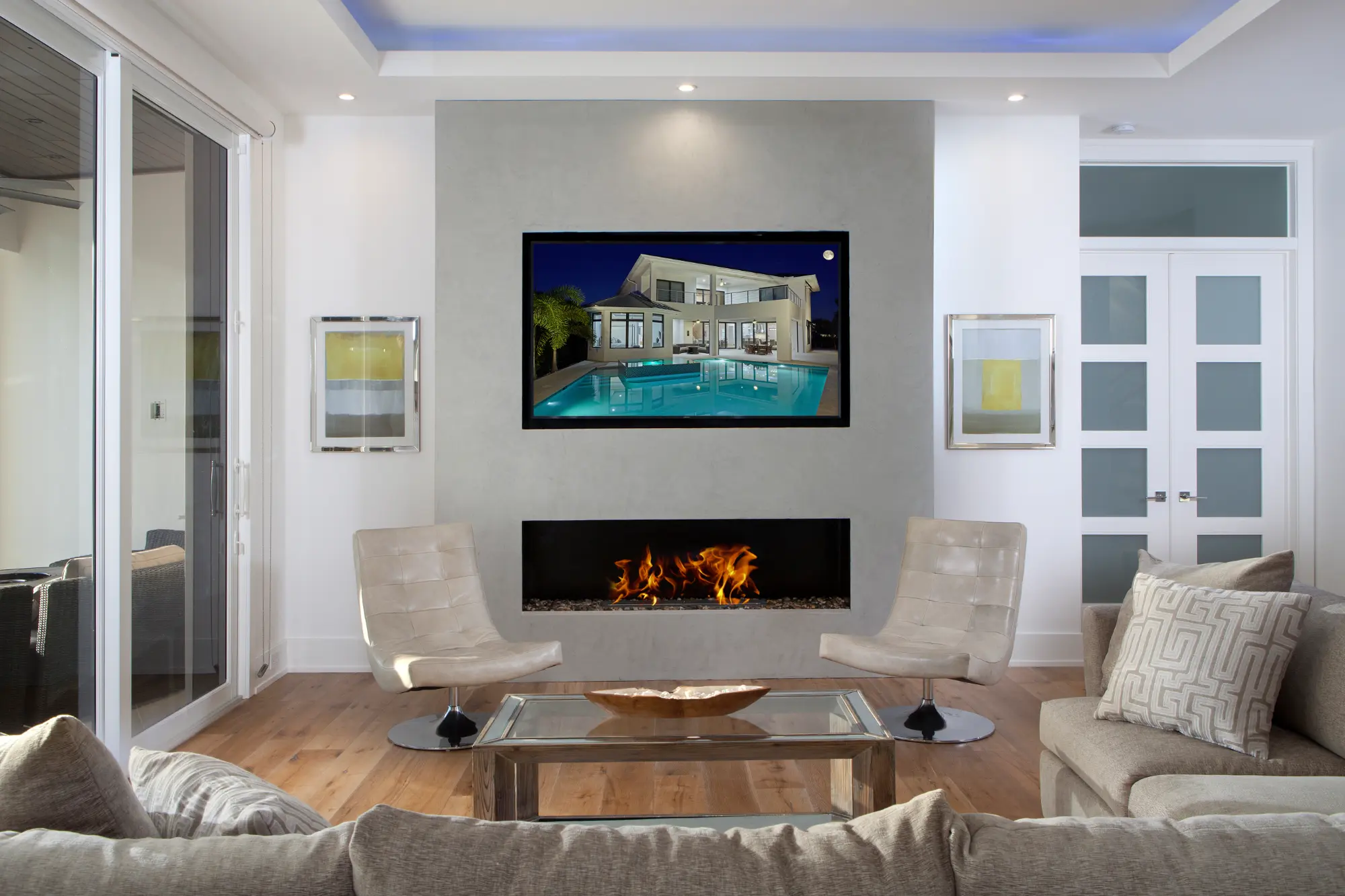 Living room with a modern fireplace, glass coffee table, and a wall-mounted TV displaying a house.