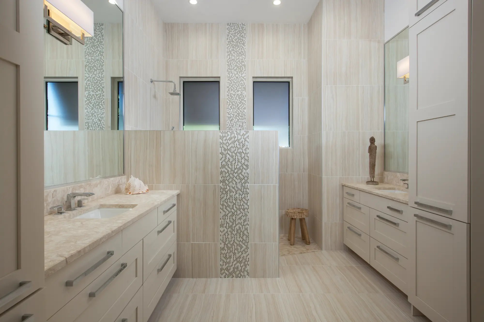 Spacious bathroom with double sinks and a walk-in shower featuring decorative tile accents.