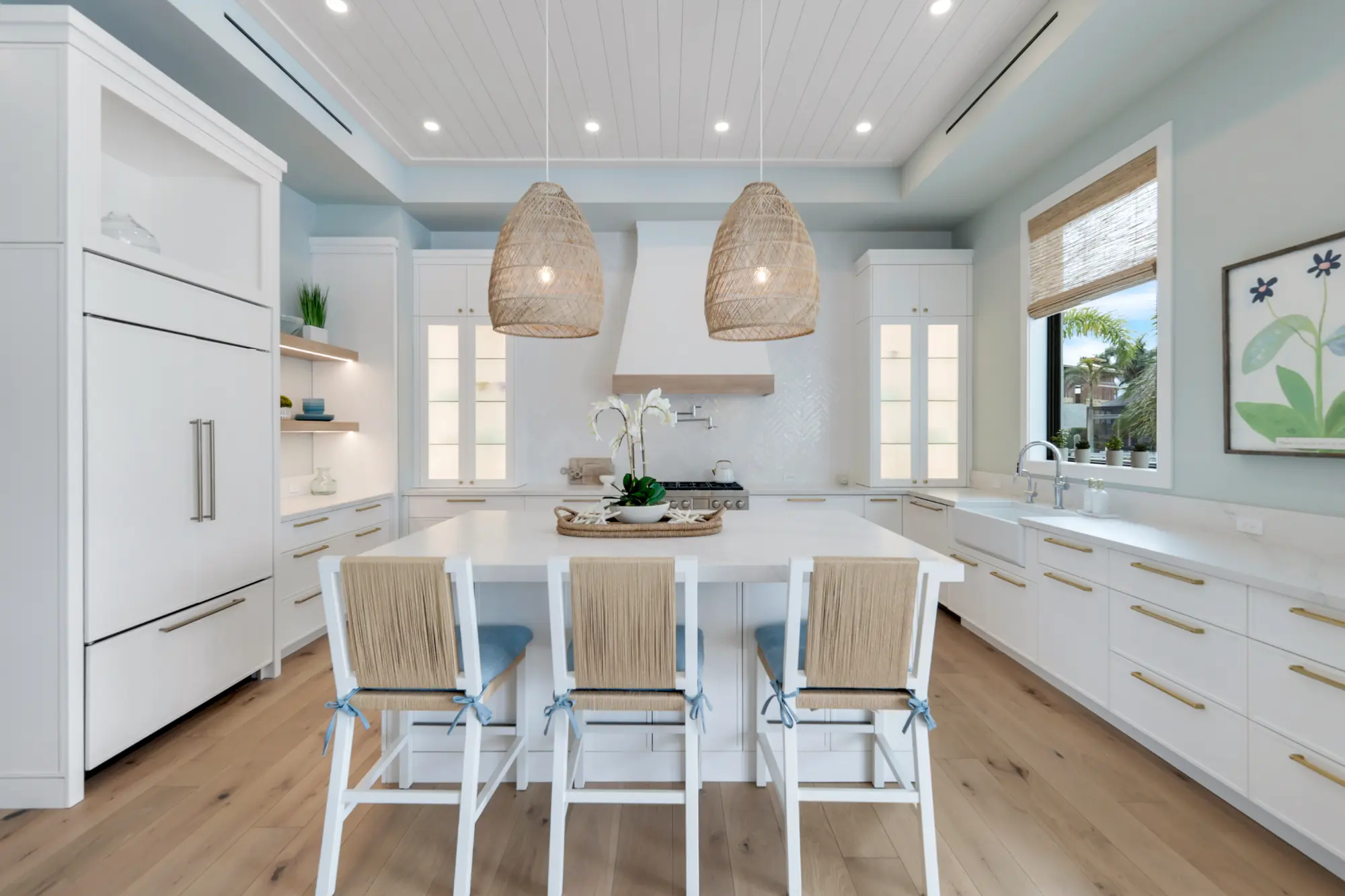 A modern kitchen with a white island, four stools, and two hanging wicker lights.