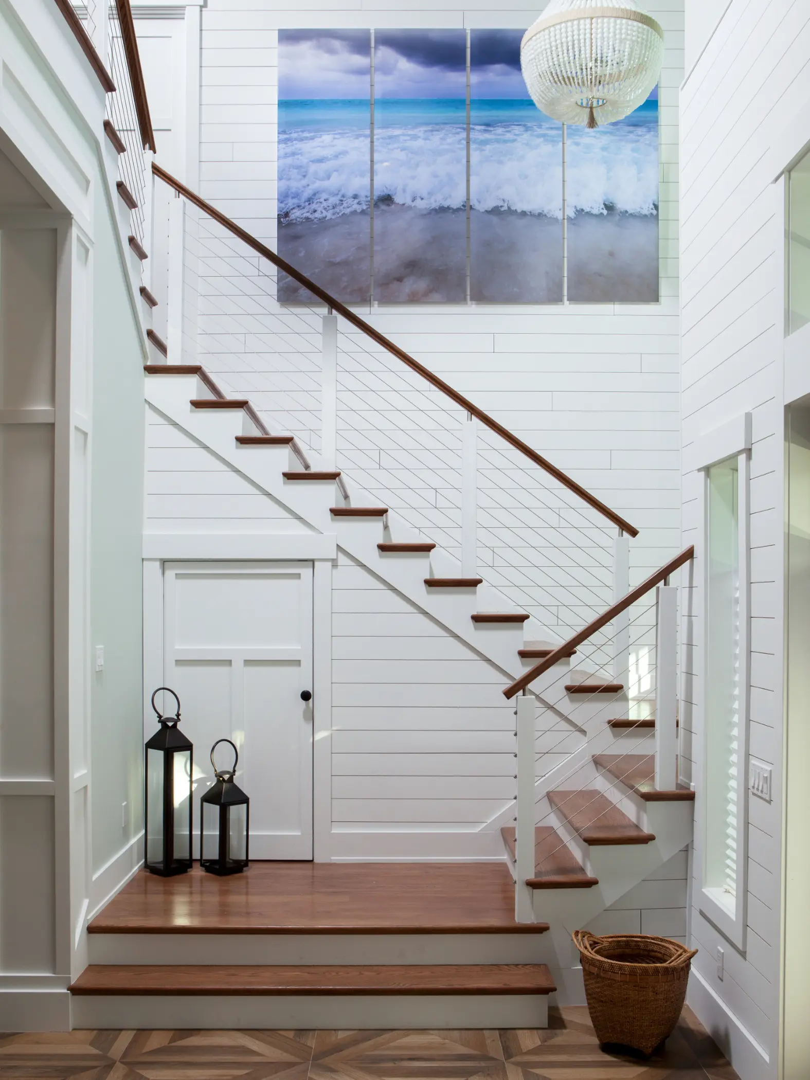 A white staircase with wooden steps, featuring a large ocean photo and a spherical light fixture.